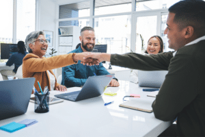 Business professionals in a modern office environment smiling and shaking hands during a collaborative meeting, illustrating the benefits of IT consulting services in fostering teamwork and strategic decision-making