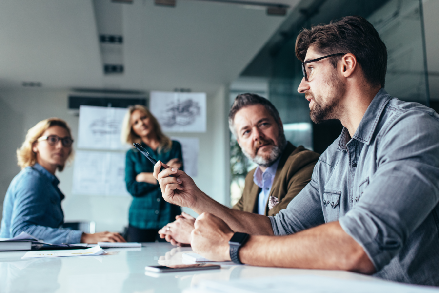 A group of professionals engaged in a discussion around a conference table in a modern office setting, illustrating the importance of streamlining business communication through collaboration and effective teamwork.
