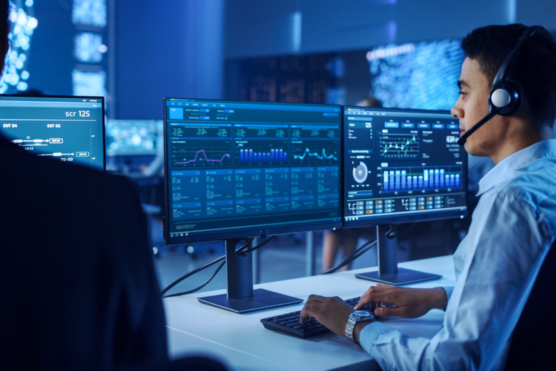 IT support specialist wearing a headset monitors multiple data dashboards in a high-tech operations center, with the text 'Understanding IT Support: When and Why Your Business Needs It' displayed—highlighting the importance of IT Support for business operations.