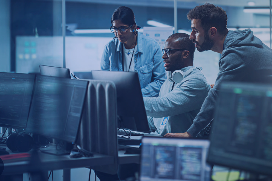 Team of IT professionals collaborating in a modern office, monitoring multiple computer screens and discussing system performance for improved IT health.